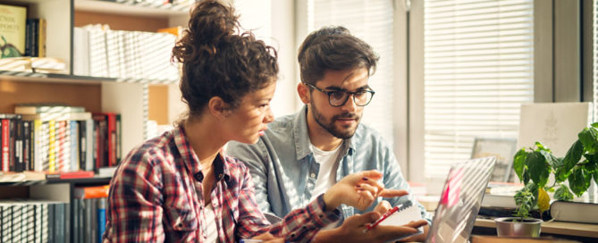 Two young modern students sitting in library and trying to solve some studying problems.
